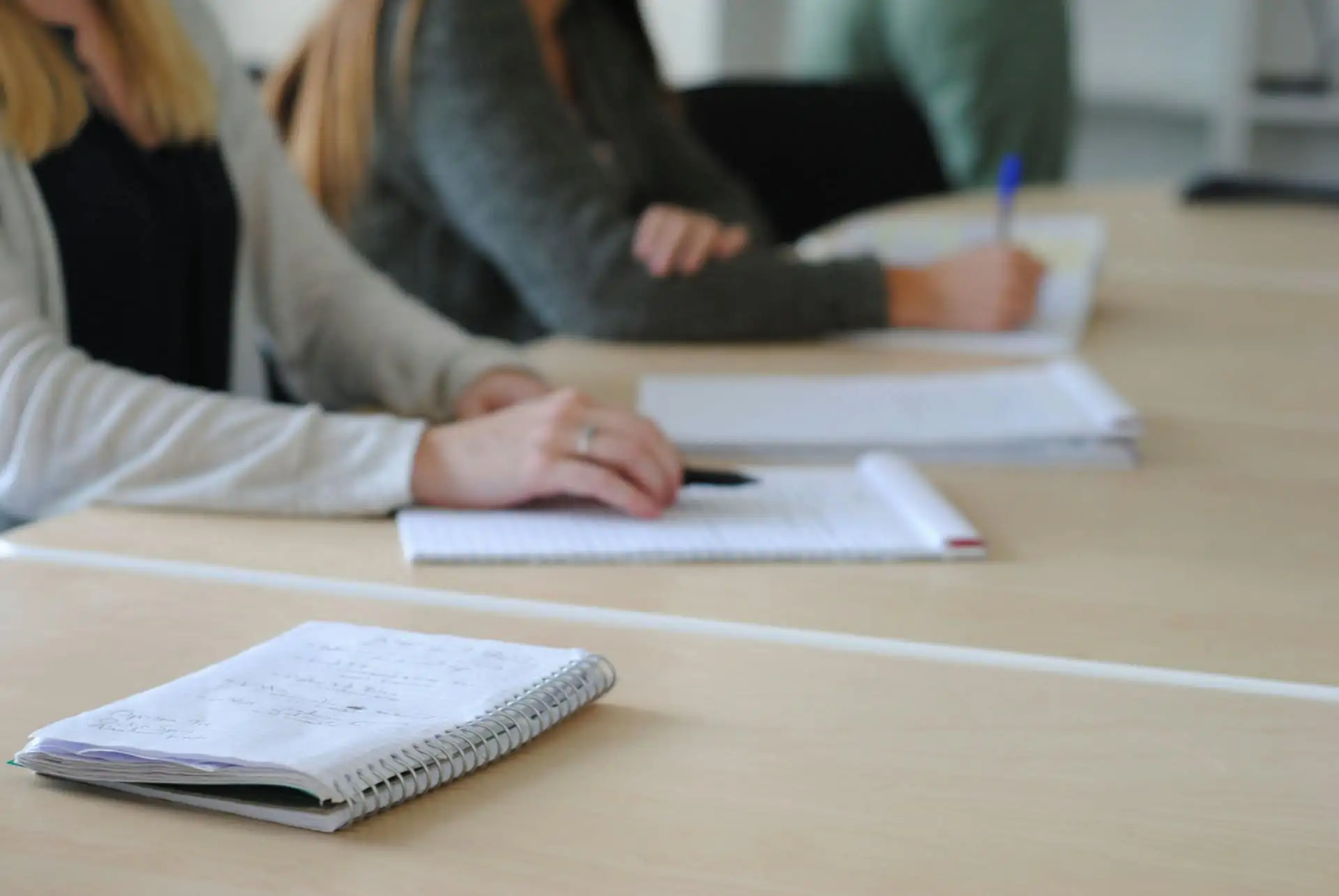 Students writing in notebooks at a shared table