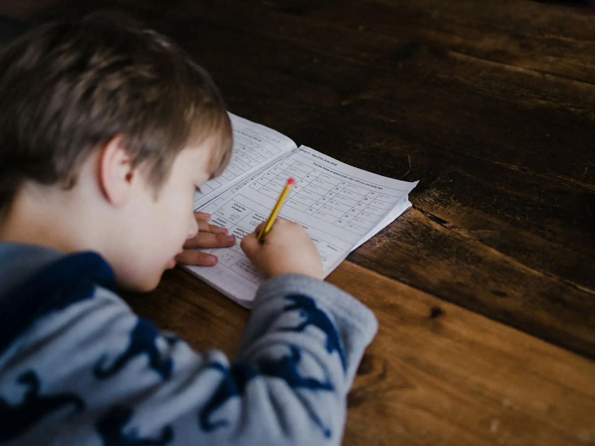 Young boy writing in an exercise book at a wooden desk