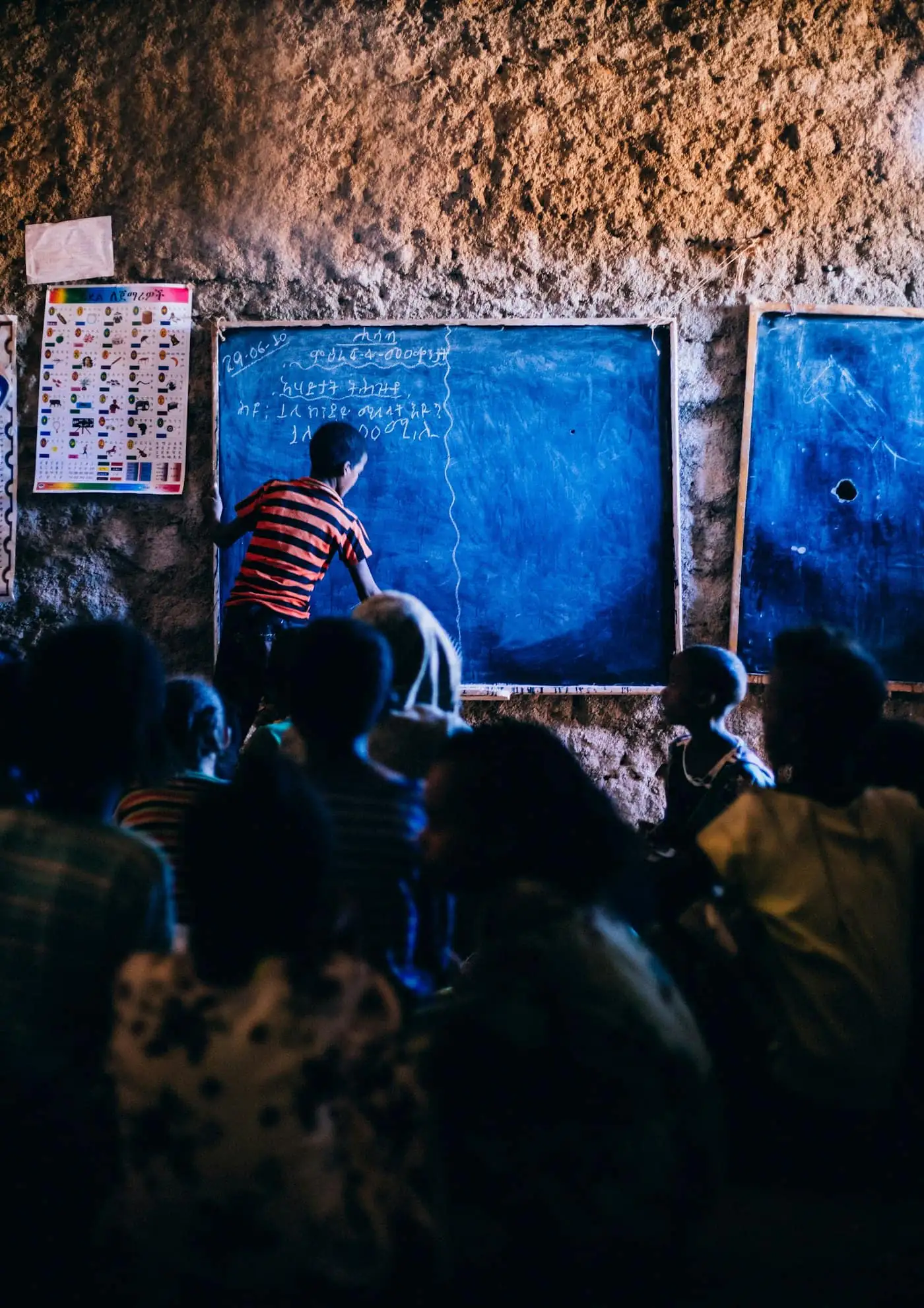 Students watching a classmate write on a blue chalkboard