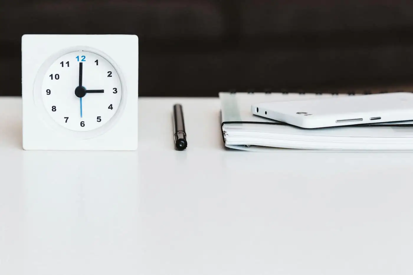 Desk clock beside a pen and a notebook