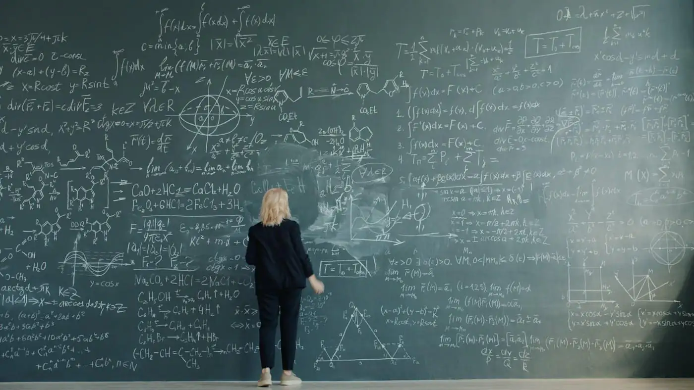 A teacher writing formulas across a large chalkboard